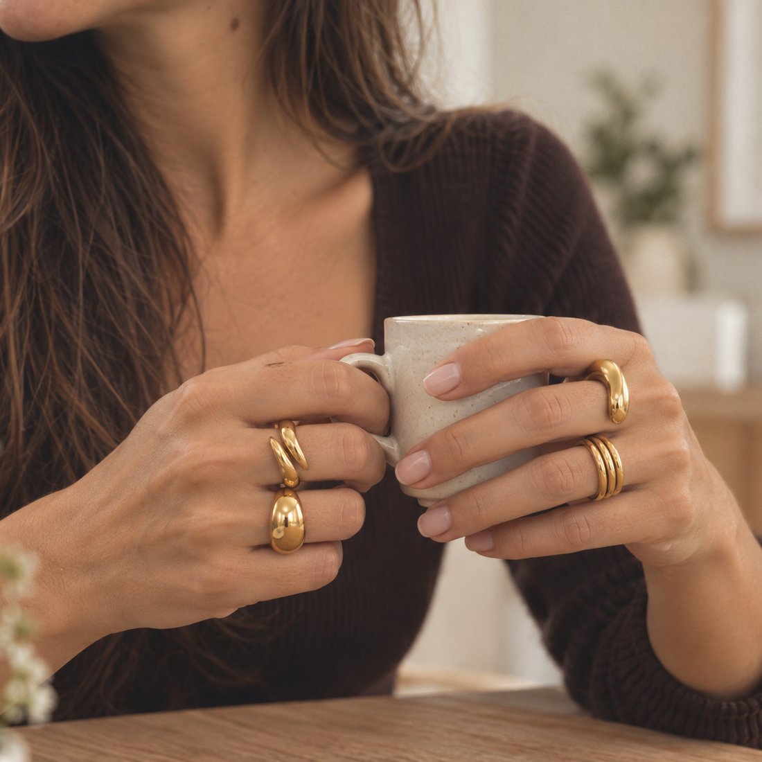 Anéis dourados nas duas mãos, à volta de uma chávena de café.