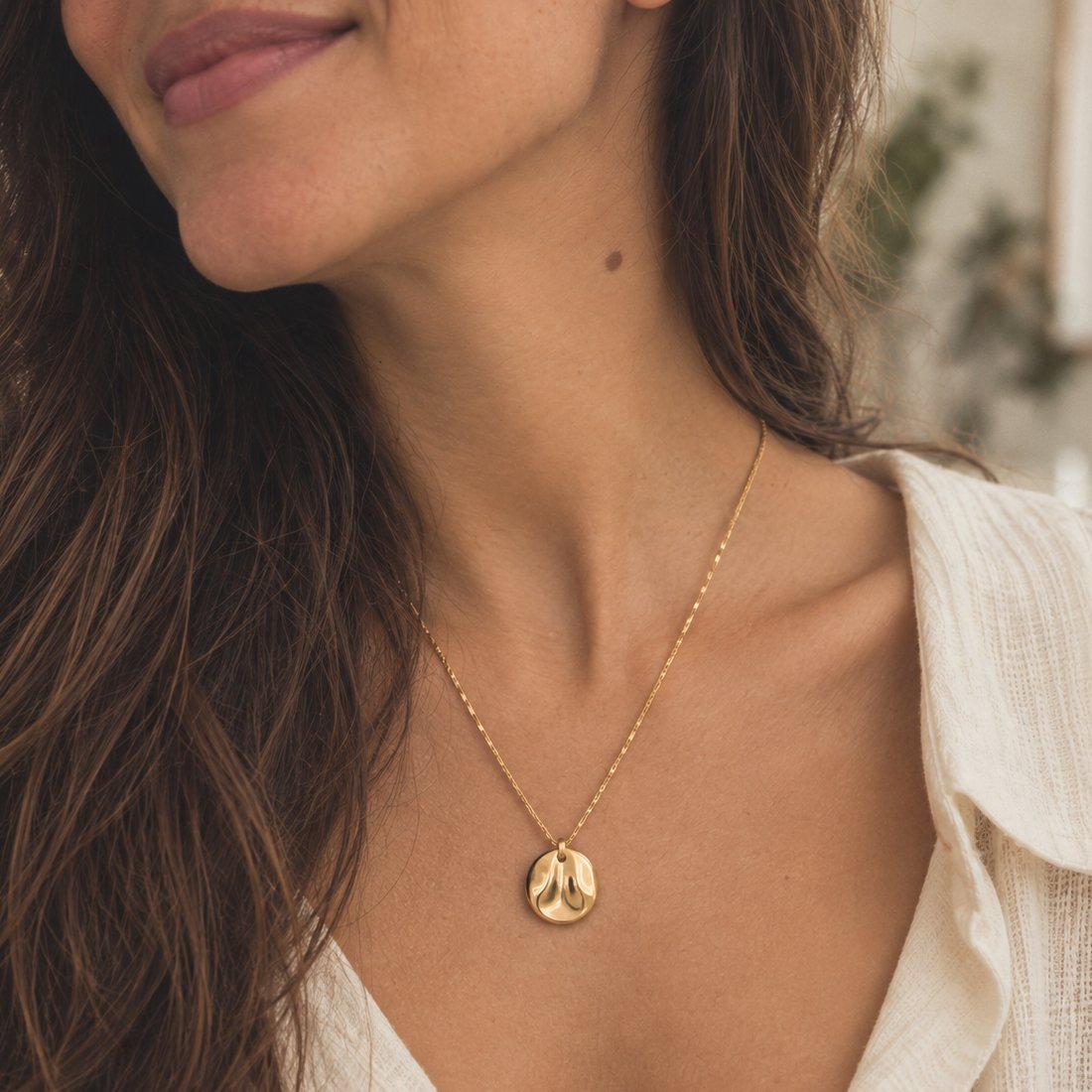 Colar dourado fino com uma medalha redonda, sobre uma camisa clara.