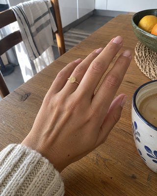 Anel dourado com medalha numa mão, à mesa do pequeno-almoço