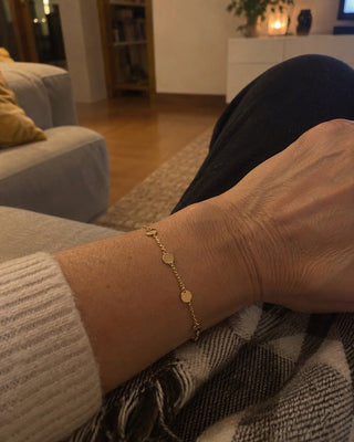 Pulseira dourada com medalhas no pulso, no sofá