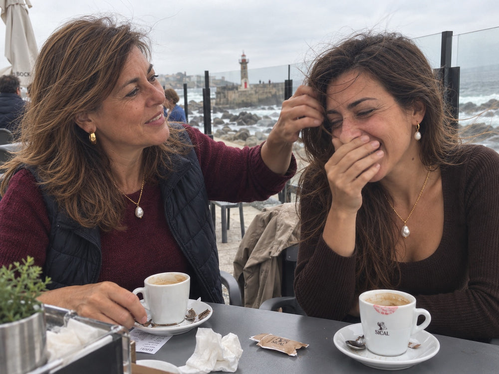 Mãe e filha numa esplanada junto ao mar, a rir, cada uma com o mesmo colar de pérola barroca.